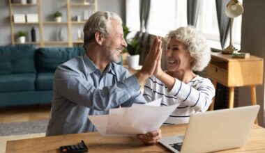 Overjoyed exited middle aged married couple giving high five, finishing doing domestic paperwork together at home. Euphoric happy older mature spouses celebrating successful investment or purchase.