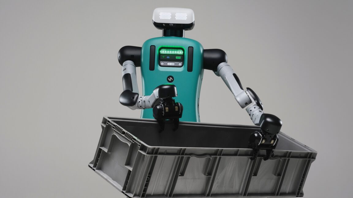 A humanoid robot with a green torso holds a large bin in two hands.