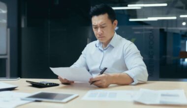 Asian man looking concerned while studying paperwork at his desk in an office
