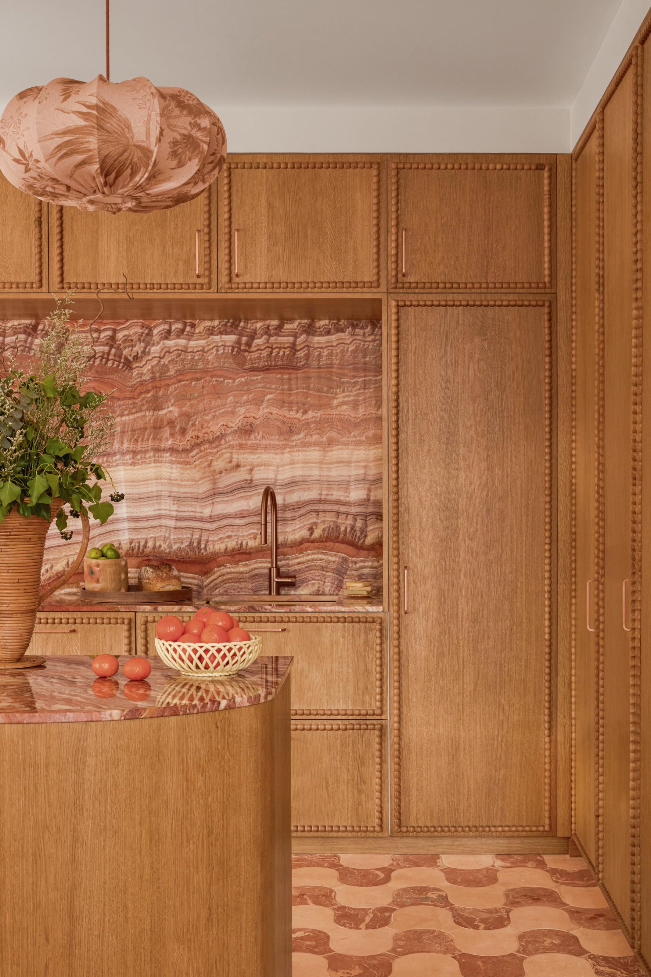 Wood kitchen with braiding around the edge of each cupboard, with pink marble backsplash and countertop and wavy pink two-tone marble tiled floor