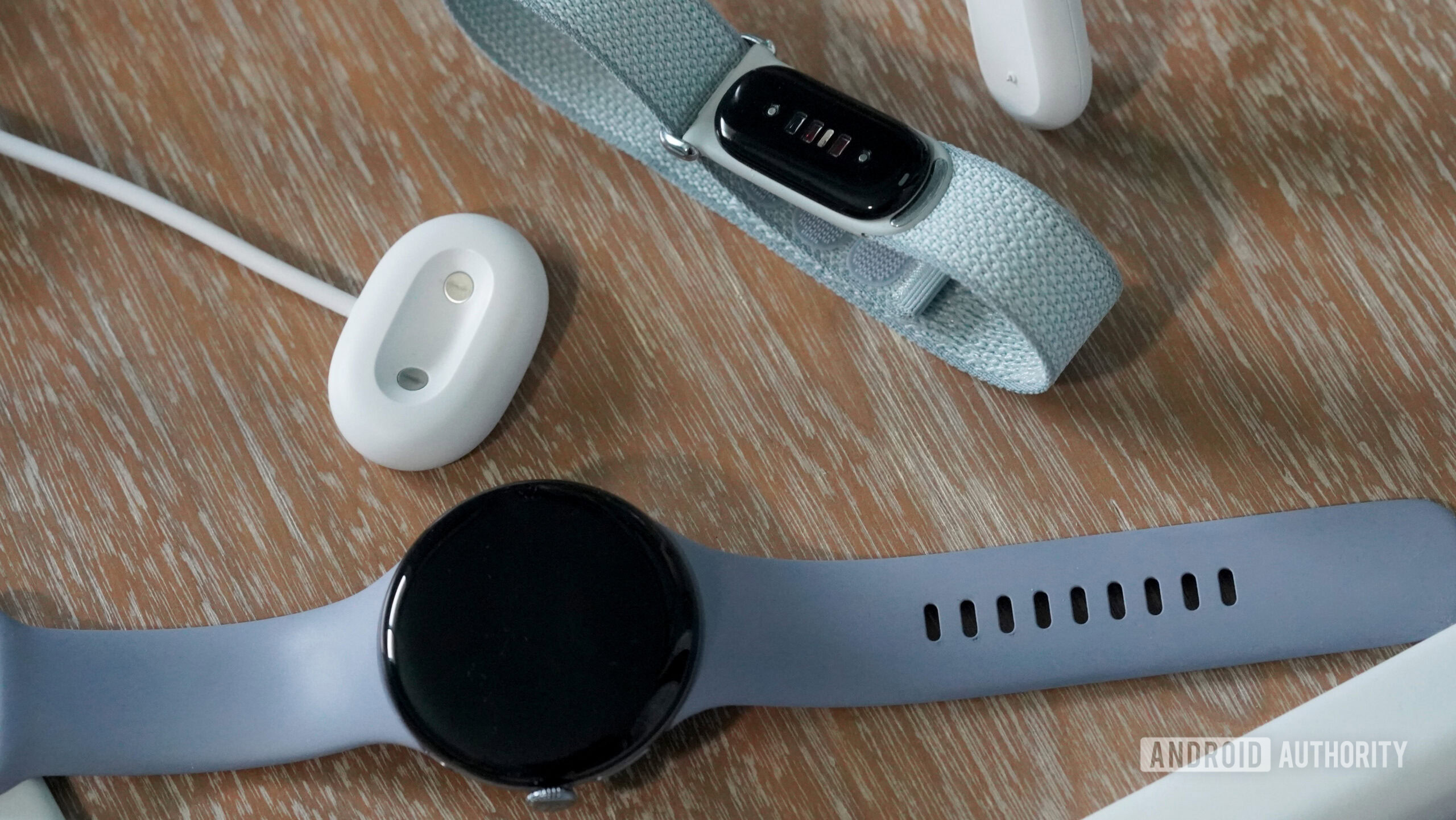 A Fitbit Air and Pixel Watch 4 rest alongside their chargers.