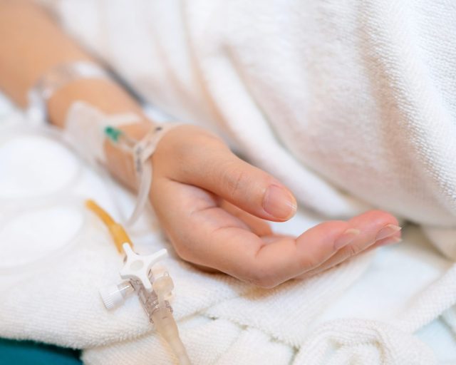 Asia patient woman lying on the bed with saline solution and syringe line on her hand in hospital ward. Emergency and treatment. Healthcare and medical concept - stock photo