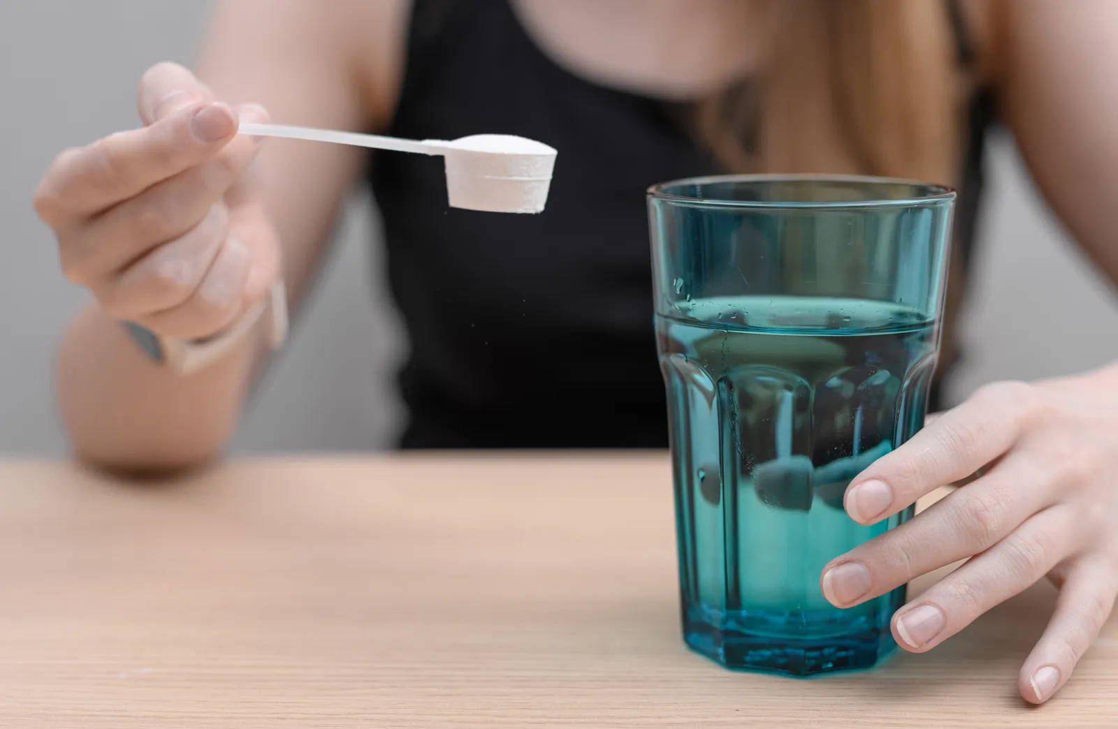 A stock image of a woman dissolving a scoop of creatine powder in water to drink.
