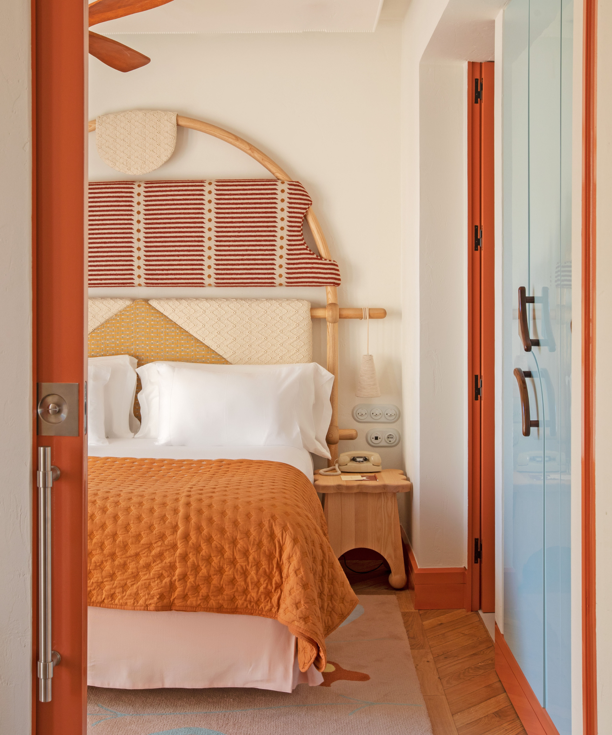 Bright bedroom with orange trim and bedding, red and white striped headboard and blue lacquered wardrobe doors