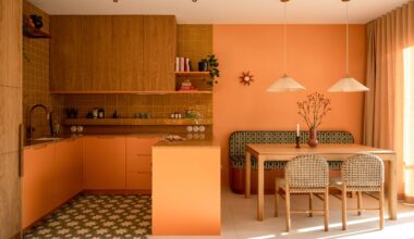 Warm-toned open-plan kitchen and dining room with orange cabinetry, oak cabinets, patterned floor tiles, woven dining chairs, and soft pendant lights