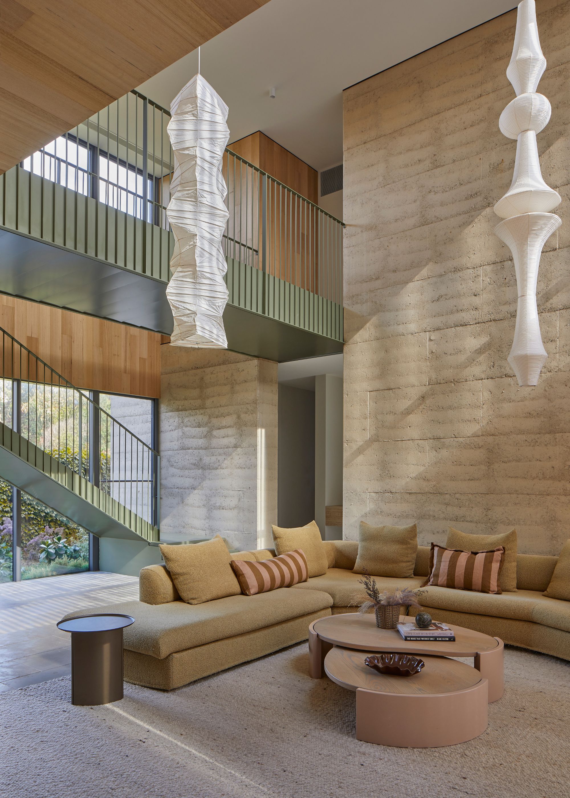 A bright open living room with two statement paper pendant lamps, a light mustard sofa, striped pillows, wood coffee tables, and a green side table