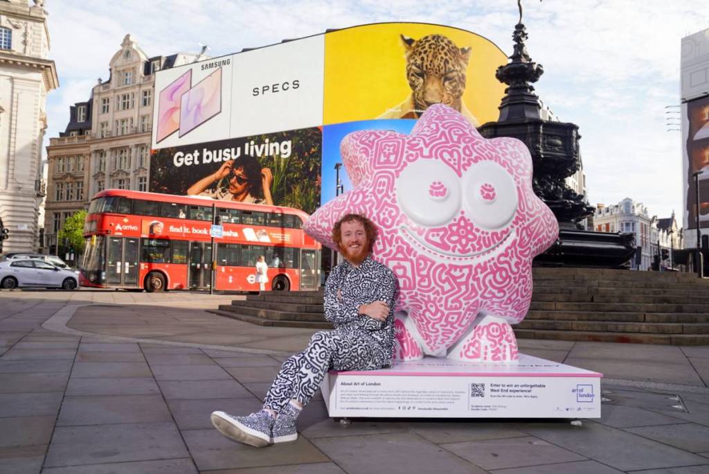 An artist stood infront of a doodled sculpture in Piccadilly Circus