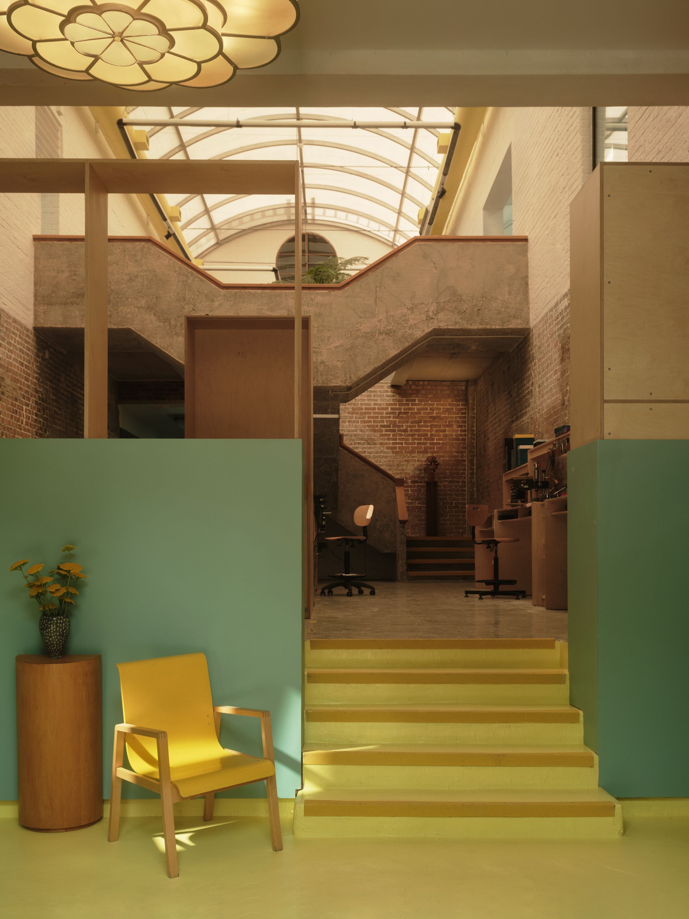 A former warehouse turned into a spectacle manufacturer's HQ, with mid-century modern furniture mixed with bold paint colors, thriving plants, desks, books, and accessories.