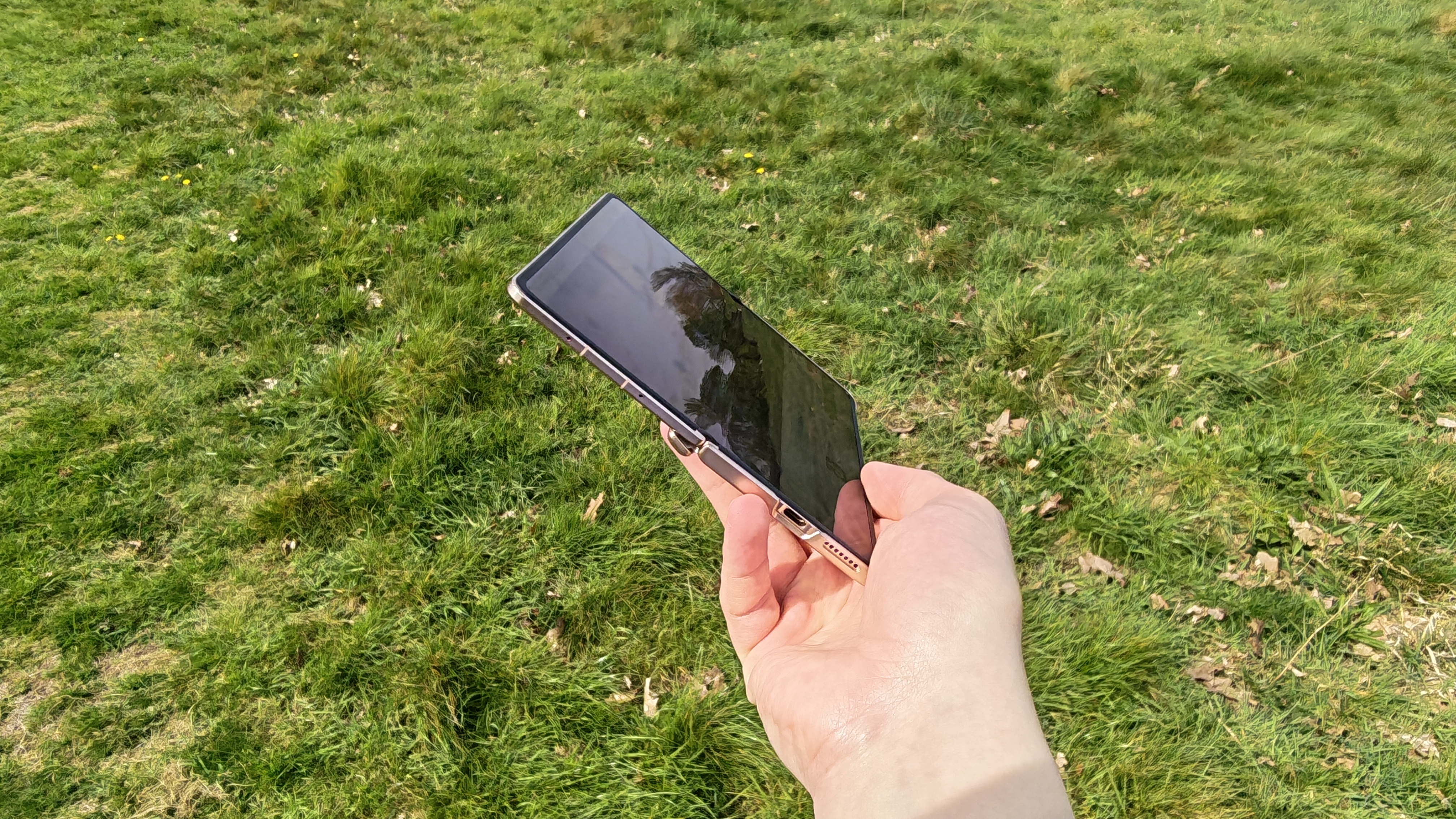 The Honor Magic V6 being held in a sunny field.