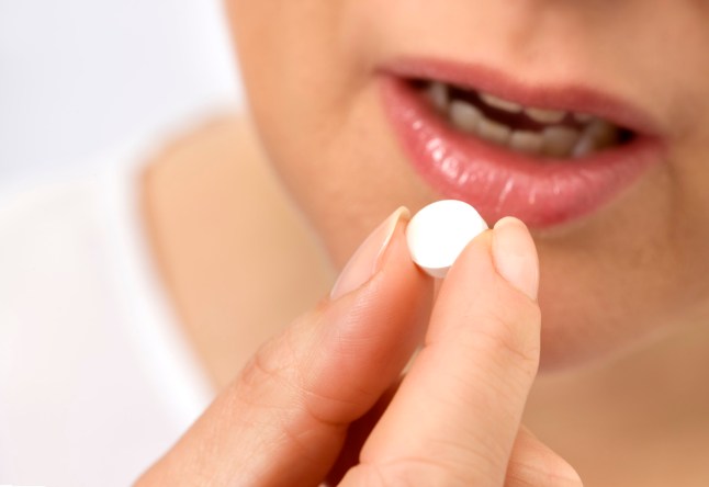 Close up image of woman holding a pill between her fingers just before placing it in her mouth
