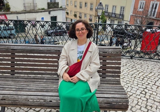 Maz Gould sitting on a wooden bench on a cobbled street, old buildings in the background (Picture: Maz Gould)