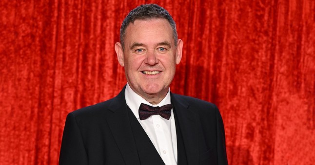 Coronation Street actor Tony Maudsley on the British Soap Awards red carpet, posing against a red curtain backdrop.