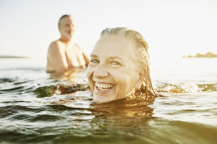 Smiling senior woman swimming with friend in bay on summer evening