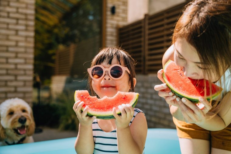 Adorable Asian little girl with sunglasses, enjoying summertime, eating fresh ripe watermelon with her mother. Summer vacation and family bonding time.