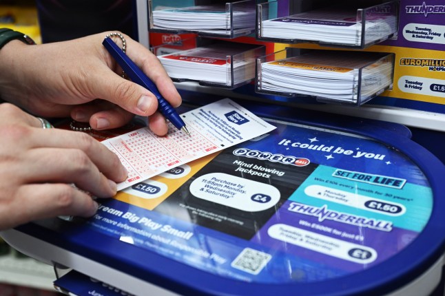 A person fills in a lottery ticket on a stand that displays the Powerball logo.