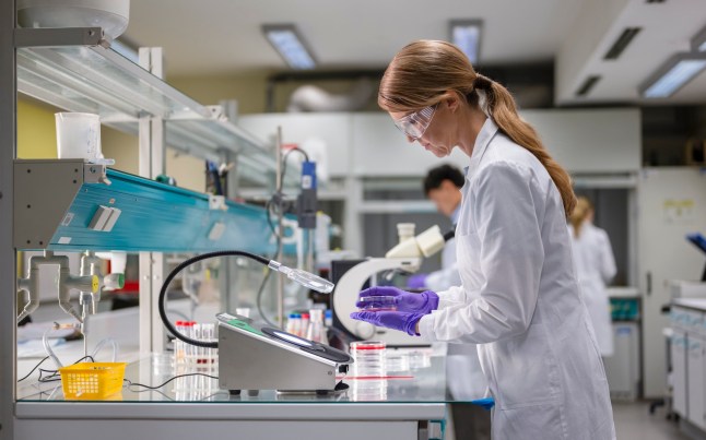 Female Scientist Performing A Scientific Experiment In A Laboratory, Holding A Petri Dish And Dropper.