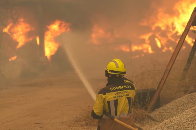 A firefighter waters burning tires and barrels while battling a wildfire in Cebreros area, near Avila, 80 kms west of Madrid on July 24, 2026. The worst wildfires in the Madrid region's history rage west of the Spanish capital, forcing authorities to evacuate or order around 40,000 people to remain indoors. (Photo by Cesar MANSO / AFP via Getty Images)