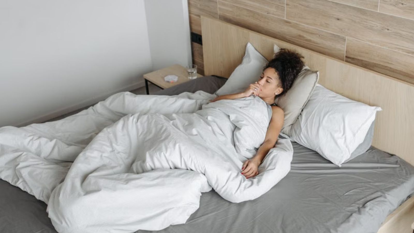 Sick woman lying in bed covered with sheets