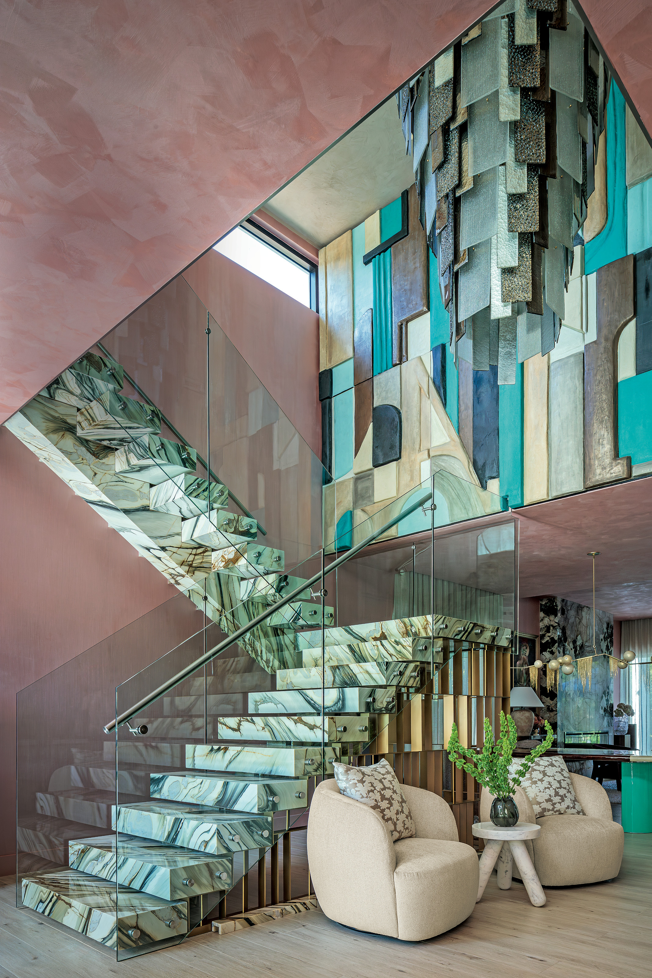 Green veined stone staircase against a pink textured wall, abstract blue and brown artwork and oversized chandelier