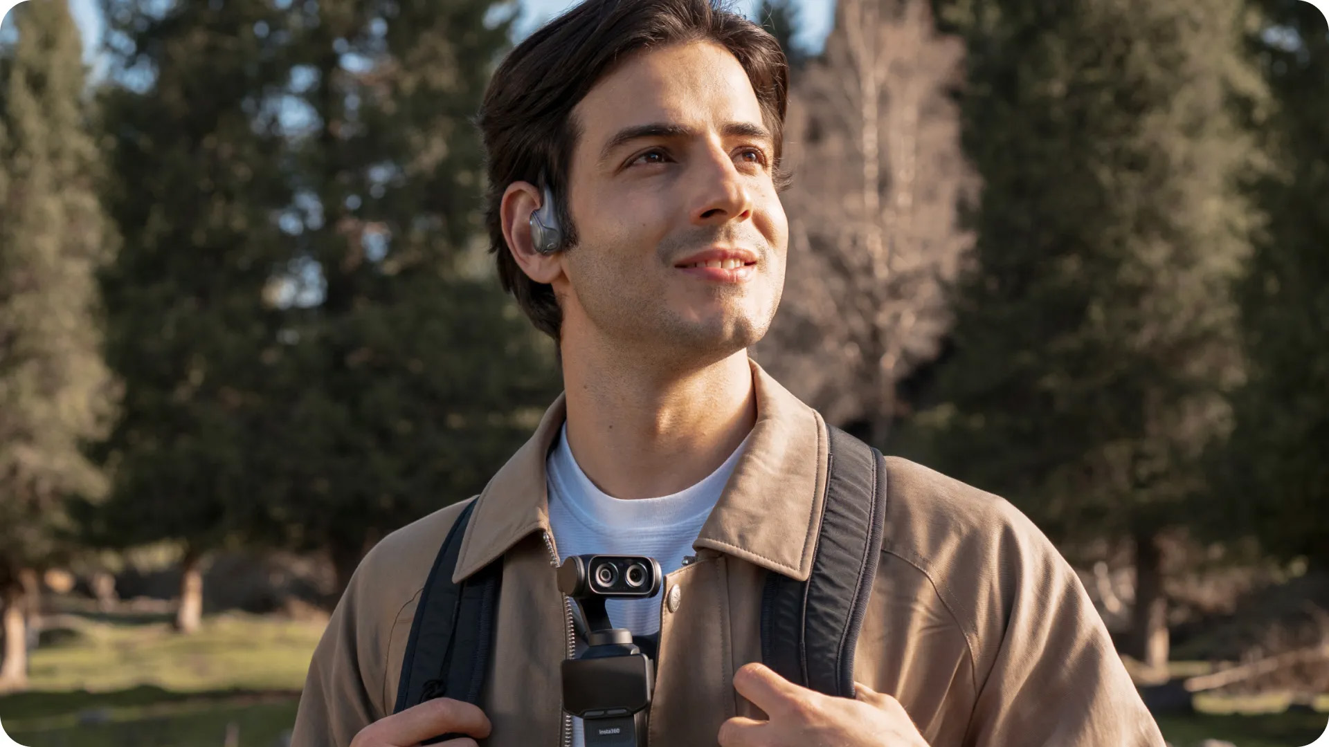 Man outdoors with Insta360 Luna Ultra around his neck on a neck strap, with Insta360 POV Head Tracker device in his ear
