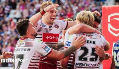 Wigan Warriors player Taylor Kerr, number 25 with his back to camera, is embraced and congratulated by team-mates after scoring a try.