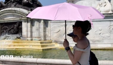A woman in a black dress uses a personal fan as she walks in the sunshine across London Bridge during a heatwave in central London.