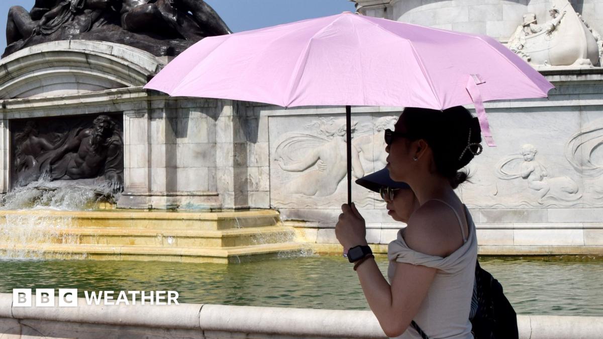 A woman in a black dress uses a personal fan as she walks in the sunshine across London Bridge during a heatwave in central London.