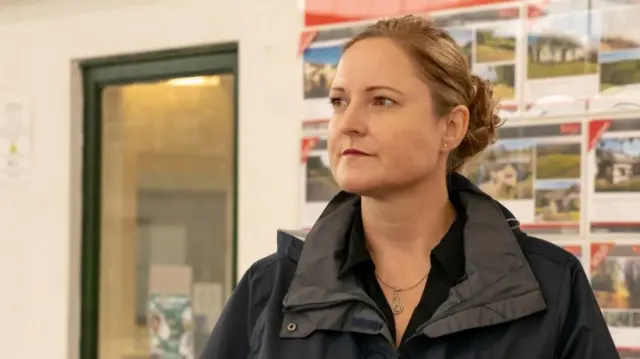 Alison Hernandez has light brown hair in a bun and wears a black waterproof coat