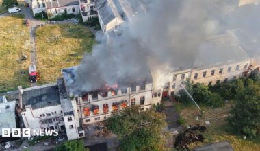 Drone shot of a burning building being hosed by firefighters.