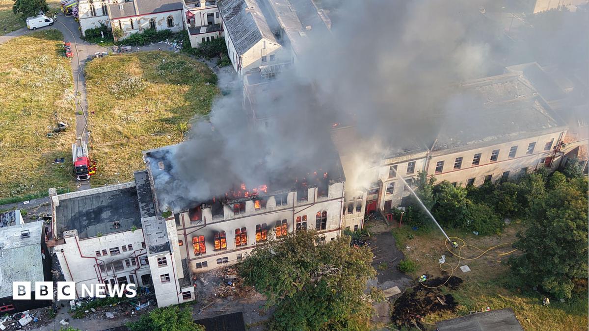Drone shot of a burning building being hosed by firefighters.