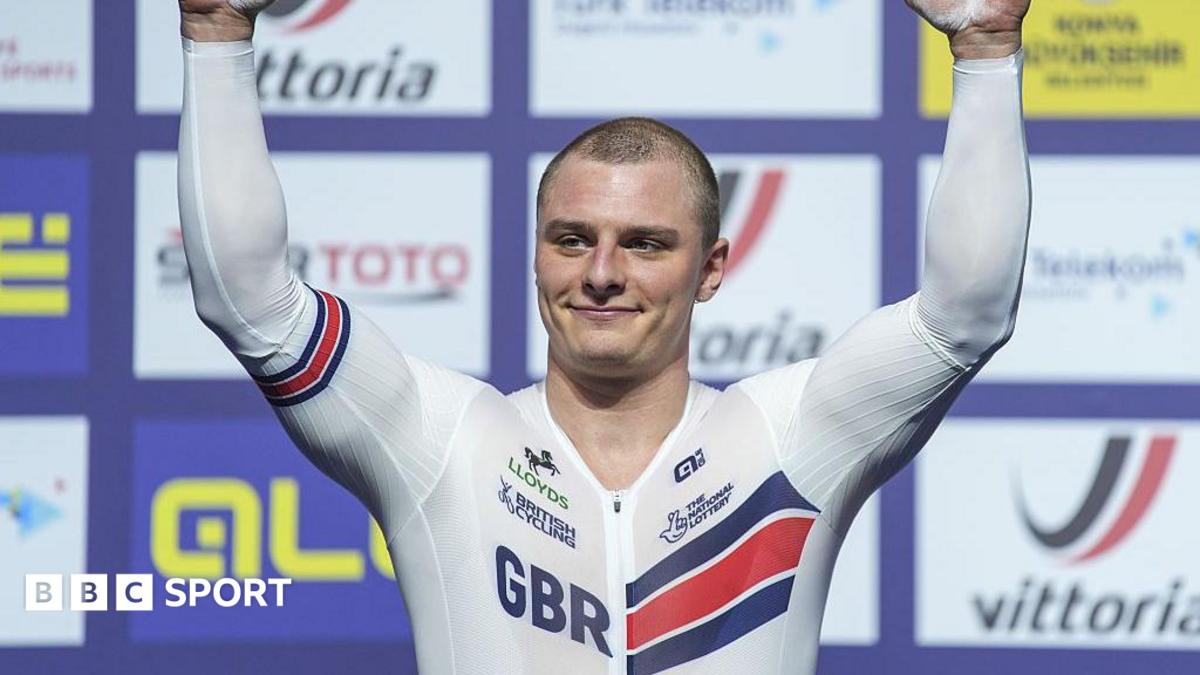 Matt Richardson in white British kit with GBR lettering raises arms aloft in front of sponsor background