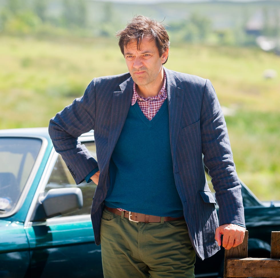 person standing beside a green car in a rural landscape.