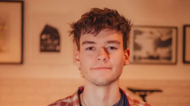 A boy with a checkered red shirt and short brown hair
