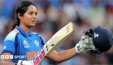 Pratika Rawal celebrates scoring a century in a One-Day international for India. She is holding up her helmet in her left hand and bat in her right. She is wearing a blue India shirt