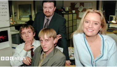 Four people (The Office UK actors) in an office all looking into the camera