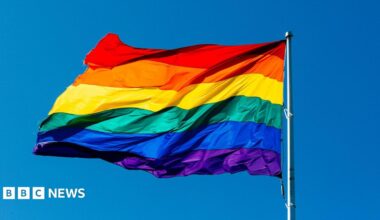 A rainbow flag is seen attached to a flag pole bearing the colours of purple, blue, green, yellow, orange and red. The flag is the universal symbol of LGBTQ pride.