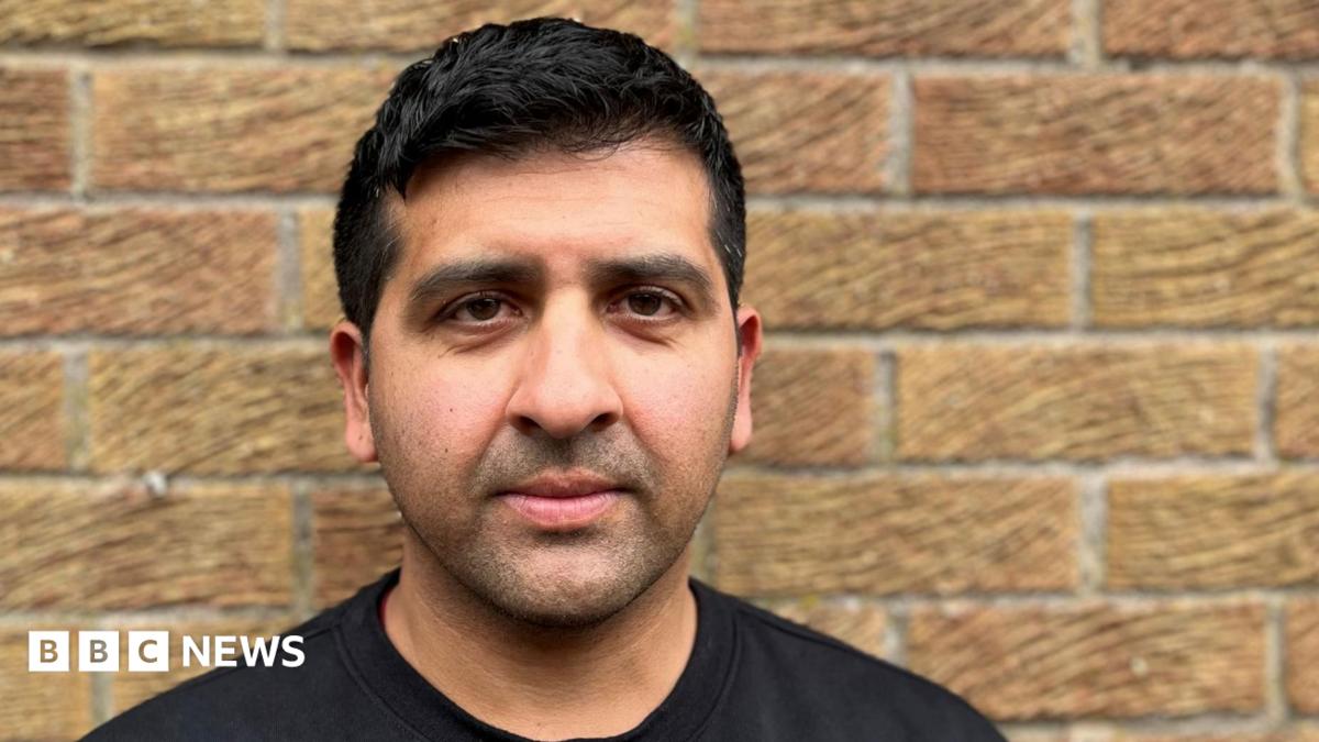 A picture of former cricketer Majid Haq. He is wearing a black T-shirt and is leaning against a brick wall, looking into the camera lens.