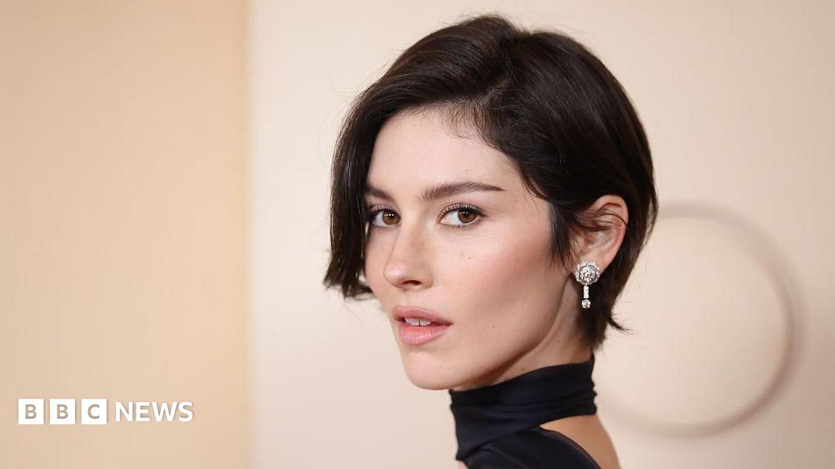 Gracie Abrams poses on the red carpet of the 2026 Oscars, in a black dress with a choker, and sparkling diamond earrings.