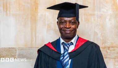 A man smiles while wearing a graduation gown and hat.