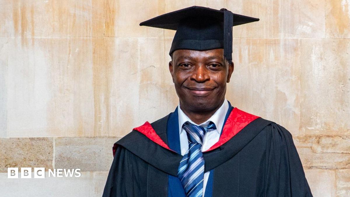A man smiles while wearing a graduation gown and hat.