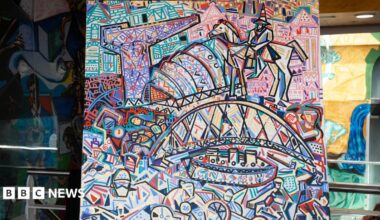 An abstract, expressionist painting of bright colours that show Glasgow's landmarks. There is a bridge, a crane and a statue painted amongst other abstract pictures. The painting is on an easel central to the photograph.