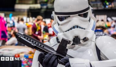 A person dressed as a stormtrooper standing in front of a crowd of people milling around stalls