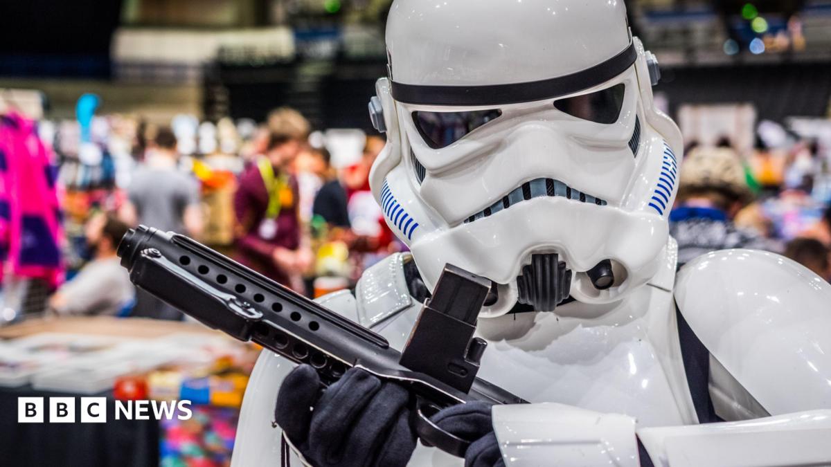 A person dressed as a stormtrooper standing in front of a crowd of people milling around stalls