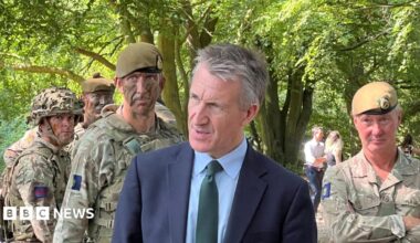 A man in a suit stood in front of people in camouflage soldier outfits.