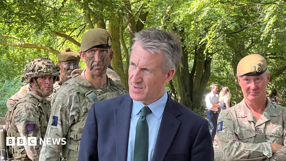 A man in a suit stood in front of people in camouflage soldier outfits.