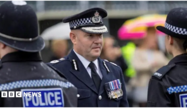 Craig Guildford, a man wearing ceremonial police uniform, looks at a line-up of police officers who are dressed in full police uniform.