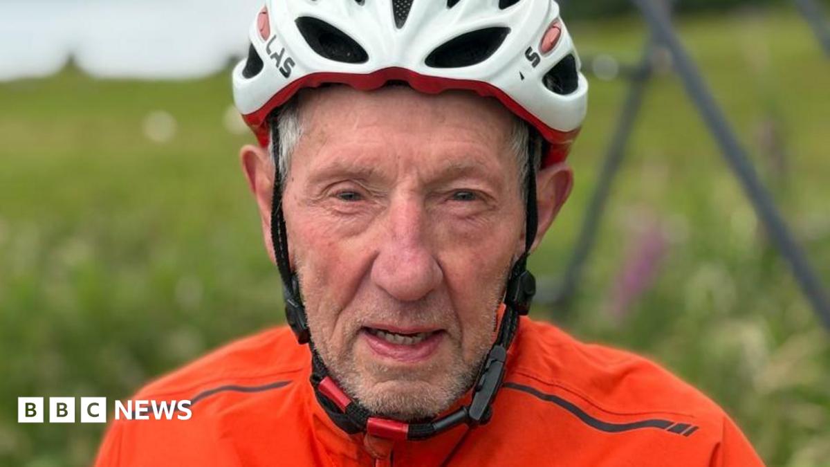 Eddie looks directly at the camera with a determined look. He's wearing a white cycling helmet and orange top.
