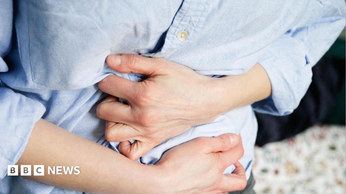 Close-up image of a person in a blue long sleeve shirt clutching their stomach.