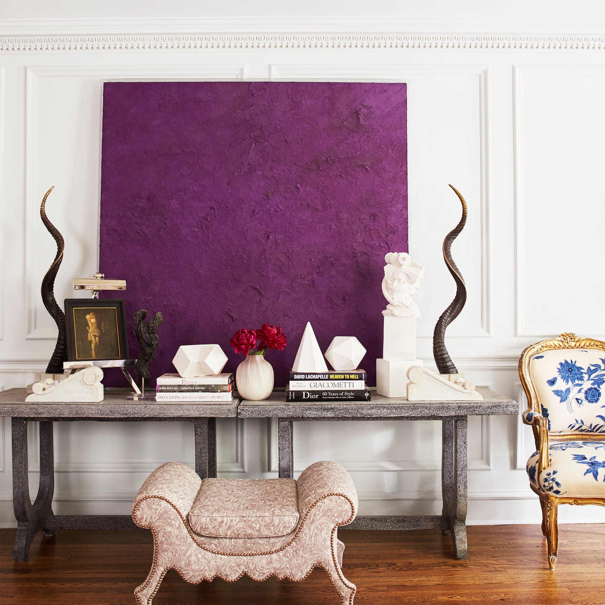 A stylish interior scene featuring a purple artwork, decorative objects, books, and elegant furniture.