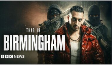 A promotional poster for a film, with an actor in the foreground in a shiny red jacket and white vest, with slicked back dark hair. Behind him are two men in balaclavas, and black clothing, holding a knife and a gun. This is Birmingham is written in white text.